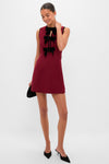 Model in Cranberry Velvet Bow Jaclyn Mini Dress, featuring classic black velvet bows, holding a black clutch, embodying an effortless, fun, and high-end style with elegant accessories.