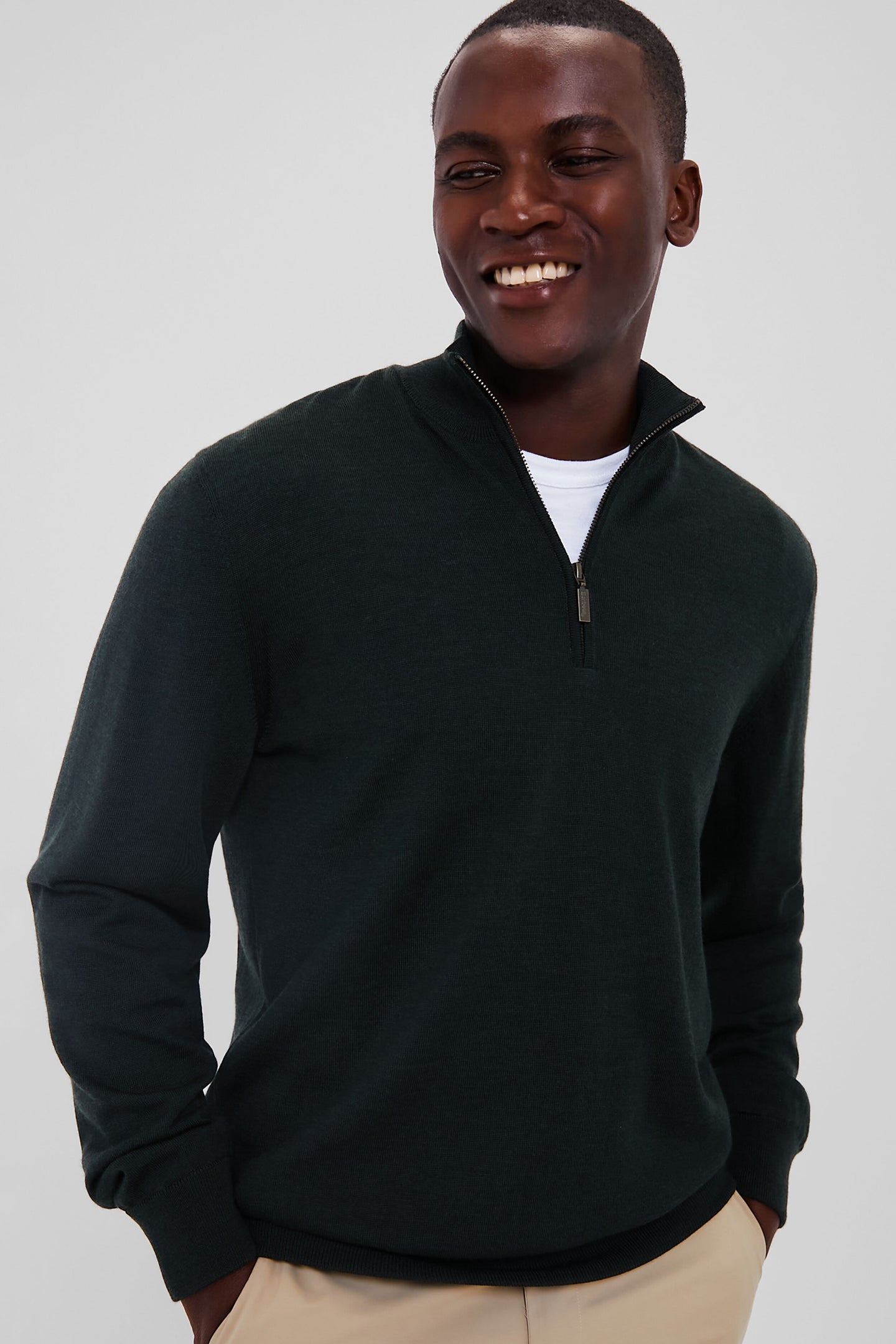 A man smiles while wearing a Barbour merino sweater with a Teflon-coated finish over a white shirt and beige pants.