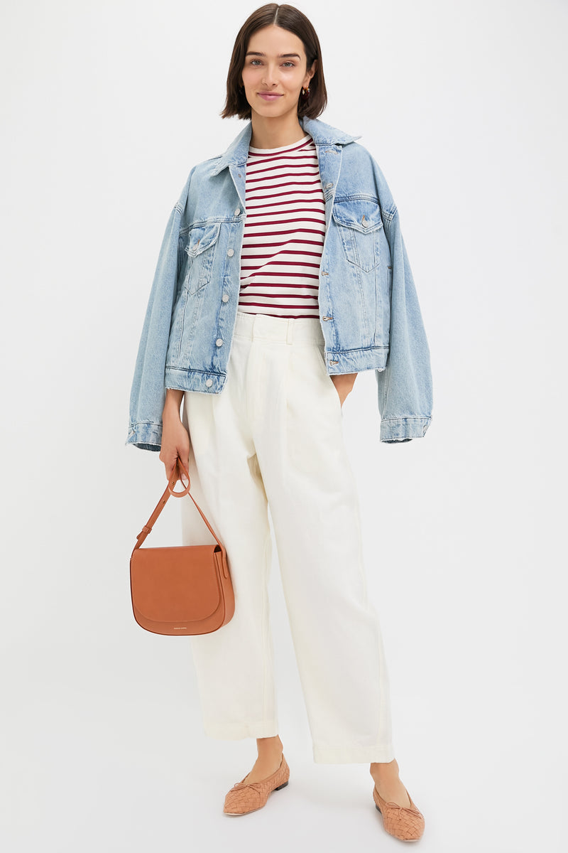 A woman in an Apiece Apart light blue denim jacket, red and white striped shirt, Cream Bari Crop Trouser, tan flats, and a brown shoulder bag stands against a plain white background.
