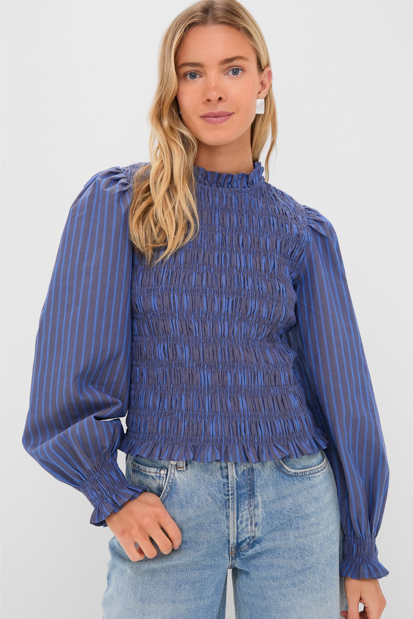 A woman wears an Oliphant blue, long-sleeve smocked bodice blouse with vertical stripes and balloon sleeves, paired with light blue jeans.