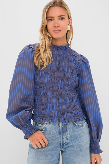 A woman wears an Oliphant blue, long-sleeve smocked bodice blouse with vertical stripes and balloon sleeves, paired with light blue jeans.