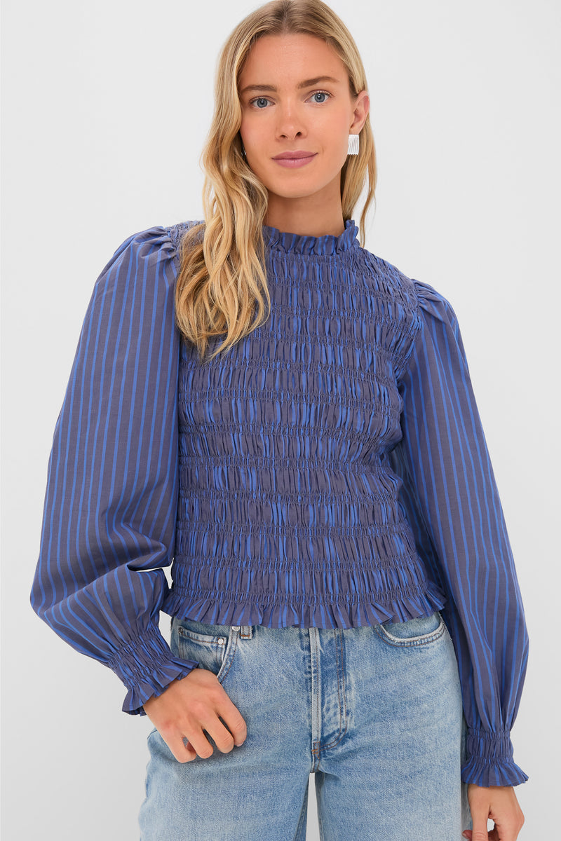 A woman wears an Oliphant blue, long-sleeve smocked bodice blouse with vertical stripes and balloon sleeves, paired with light blue jeans.