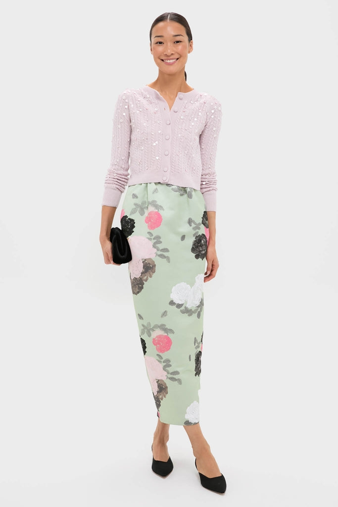 Woman models the classic Blush Pink Gilberte Embroidered Cardigan, paired with a floral pencil skirt, black clutch, and flats, embodying an effortless, high-end, and fun spring look.