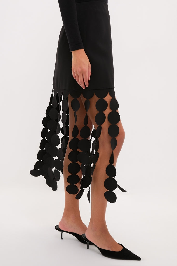 Model wears the Black Multi Circle Mercedes Maxi Skirt with dangling circular cut-outs, styled with a classic black top and pointed-toe mule heels for an effortless, high-end look.