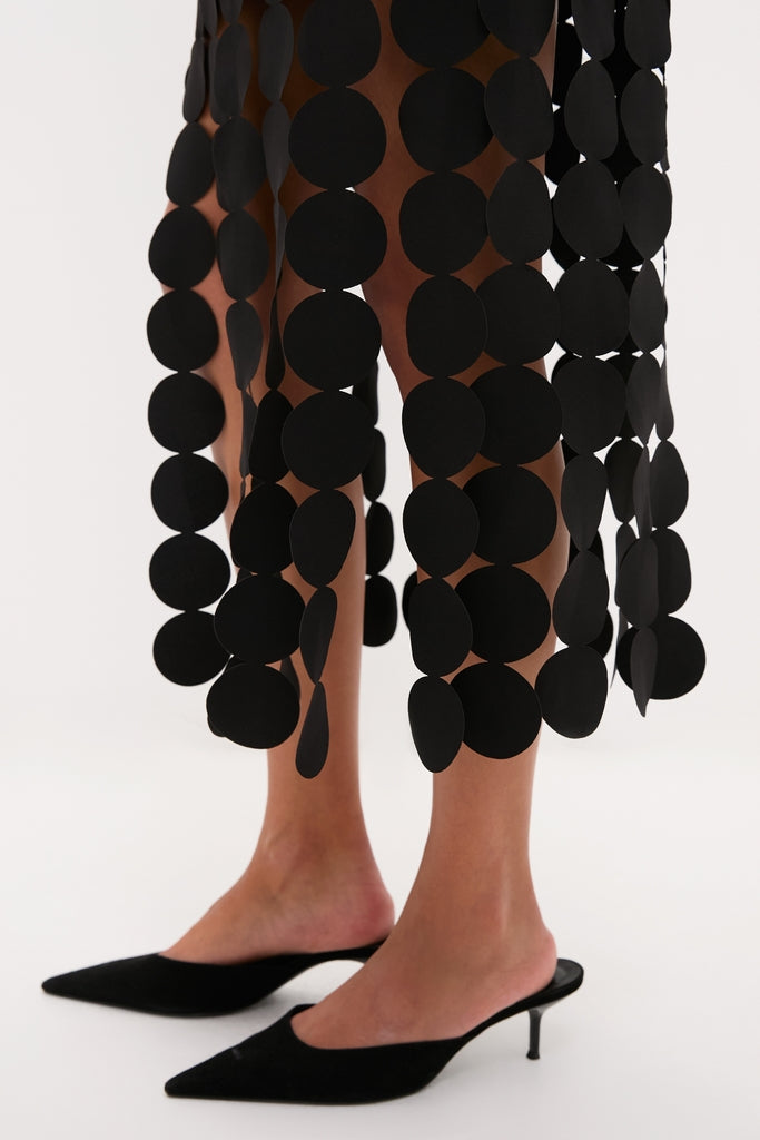 Model's lower legs in Black Multi Circle Mercedes Maxi Skirt with oversized paillettes, paired with classic black pointed-toe mule heels for an effortless, high-end look.