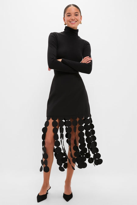 Woman wearing Black Multi Circle Mercedes Maxi Skirt with a unique circle fringe, paired with a classic black turtleneck, embodying effortless, high-end style.