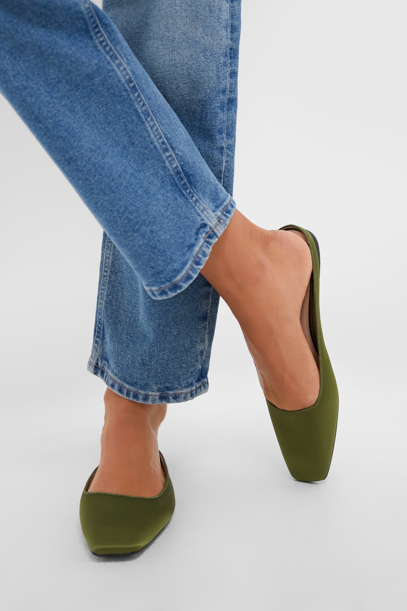 Person wearing classic Fern Satin Nilli Flats with a square toe and mule silhouette, styled effortlessly with blue jeans for a fun, high-end look.