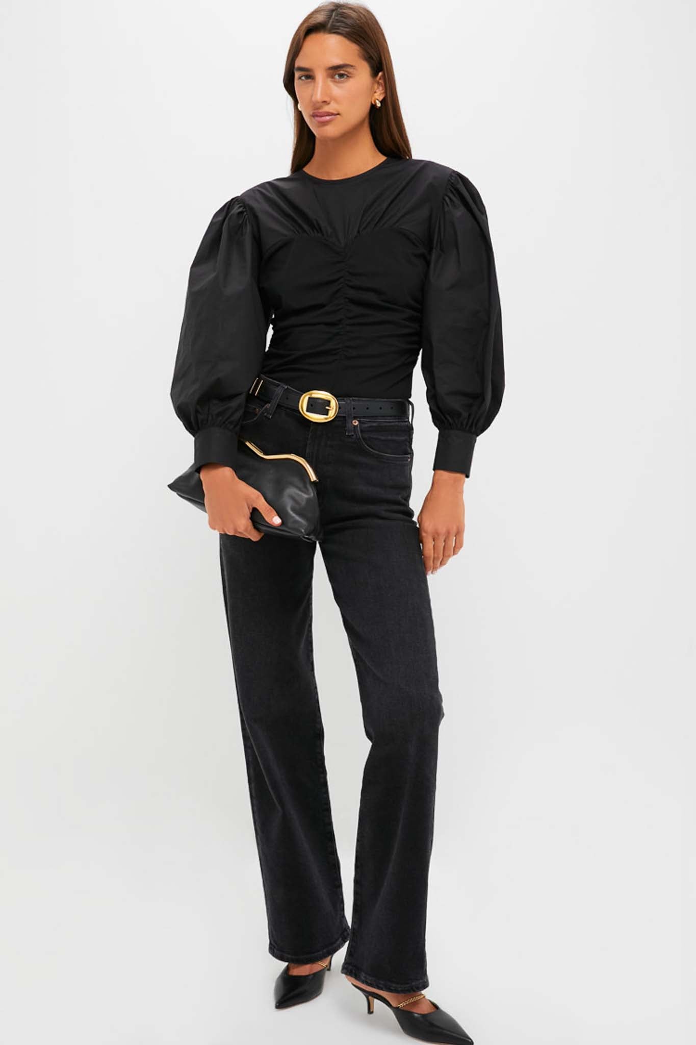 A woman models a Hyacinth House black mixed-media blouse with balloon sleeves, paired with dark jeans, black heels, and a black clutch bag, standing against a plain light background.