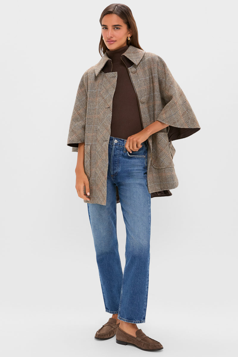Woman models the Herringbone Stewart Poncho: a classic, effortless cape-like coat over a ribbed turtleneck, paired with jeans and loafers for a high-end, fun fall style.