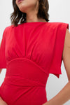 A woman wears an Andres Otalora dress in vibrant red, featuring structured sleeves and a textured, ruched waistband.