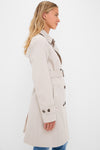 Blonde woman models Mist Short Greta Showerproof Jacket; classic trench with effortless high-end design, featuring double-breasted front, tortoiseshell buttons, and removable belt.