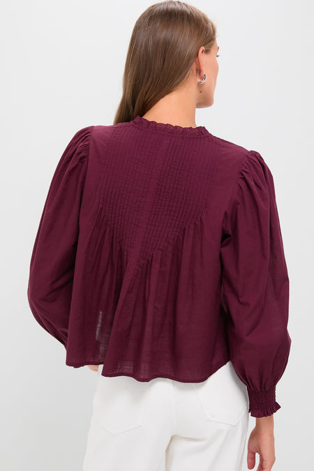 Woman in high-waisted white pants wearing the Exclusive Burgundy Anise Long Sleeve Top, featuring pintucked details and a slightly flared silhouette, exuding classic, effortless style.