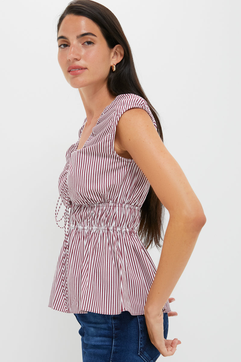 Young woman in profile wearing the Burgundy Maia Stripe Hedda Top with a ruched waist and peplum hem, effortlessly paired with dark jeans.