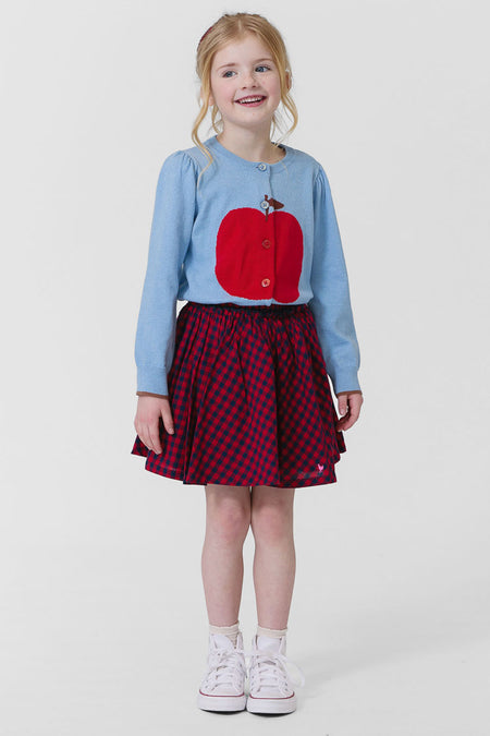 Young girl in a classic, light-blue Apple Constance Sweater with gathered puff shoulders, paired with a fun checkered skirt and high-end white sneakers. Effortlessly cool and confident look.