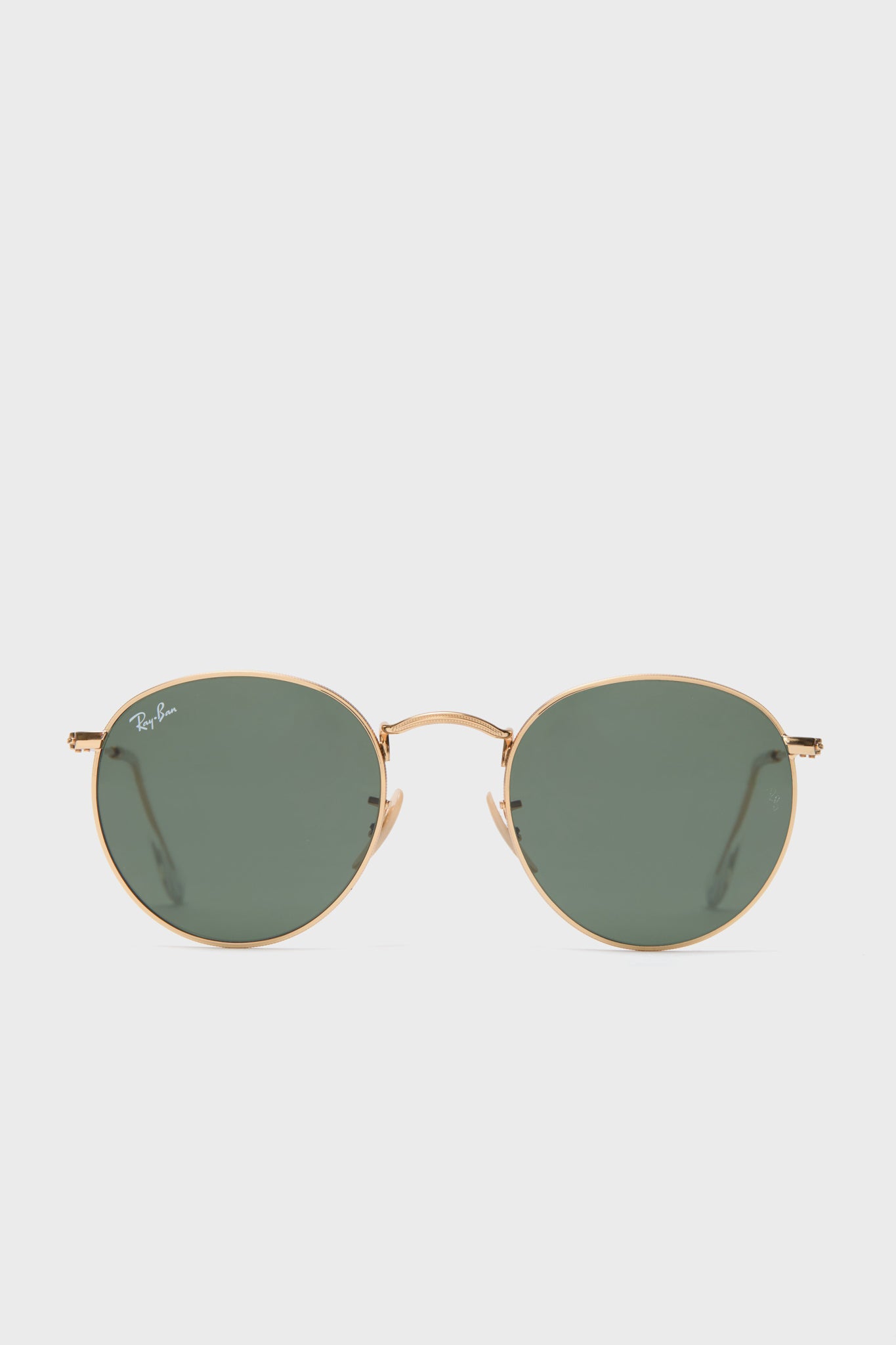 A pair of Ray-Ban round sunglasses with a gold frame and green-tinted lenses is displayed.