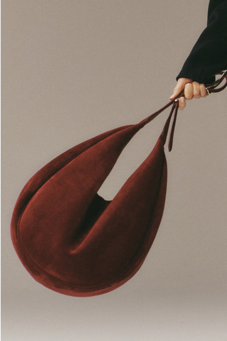 Hand holding the classic, high-end Maroon Suede Moon Hobo; a teardrop-shaped, effortlessly chic handbag with a slender strap, perfect for fun, everyday use.