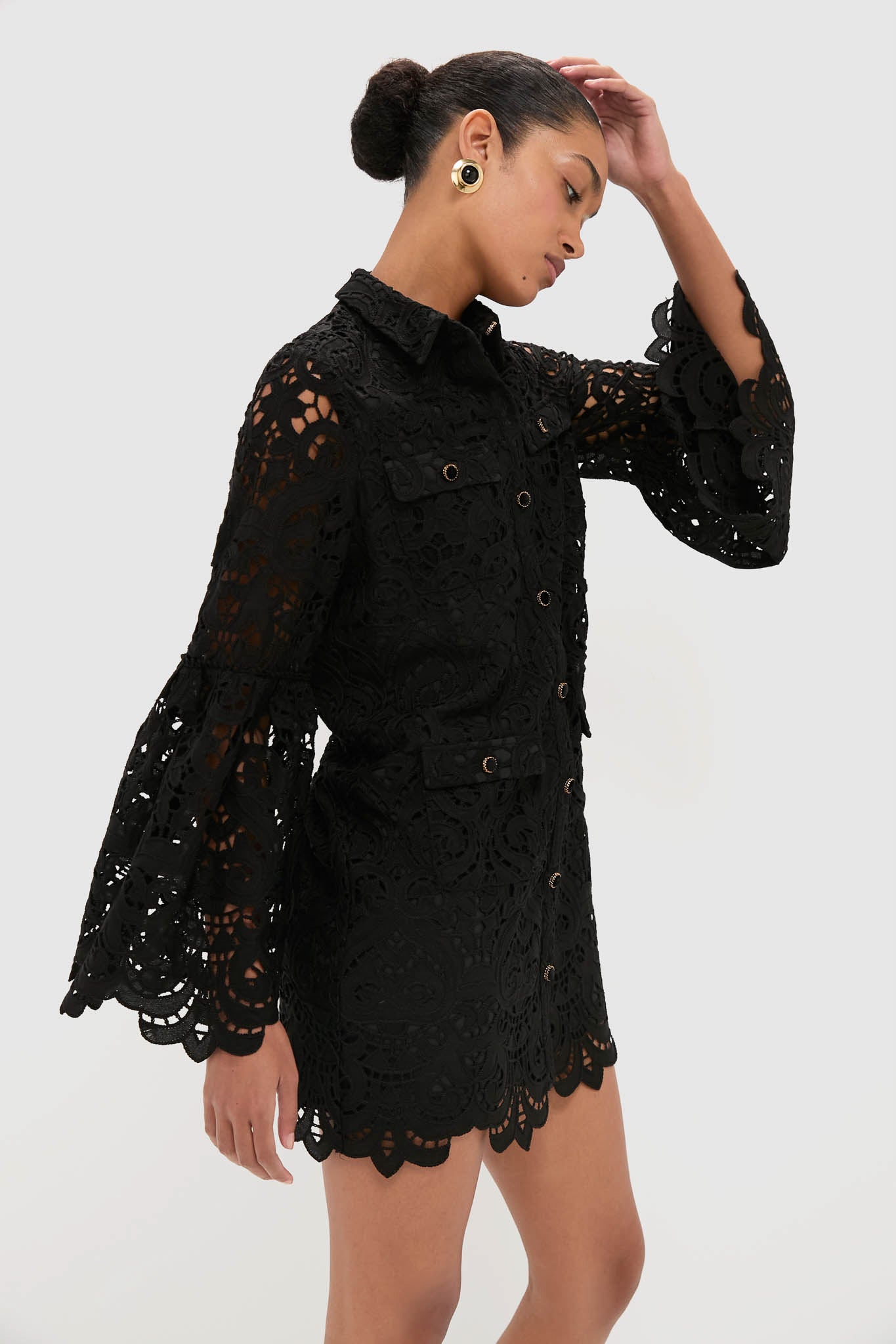 Model in profile wearing the Black Lace Long Sleeve Rachael Mini Dress, showcasing its classic, effortless design with scalloped detailing, gold buttons, and flap pockets.