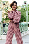 Woman standing in front of a metro in a pink striped blouse and pant set. 
