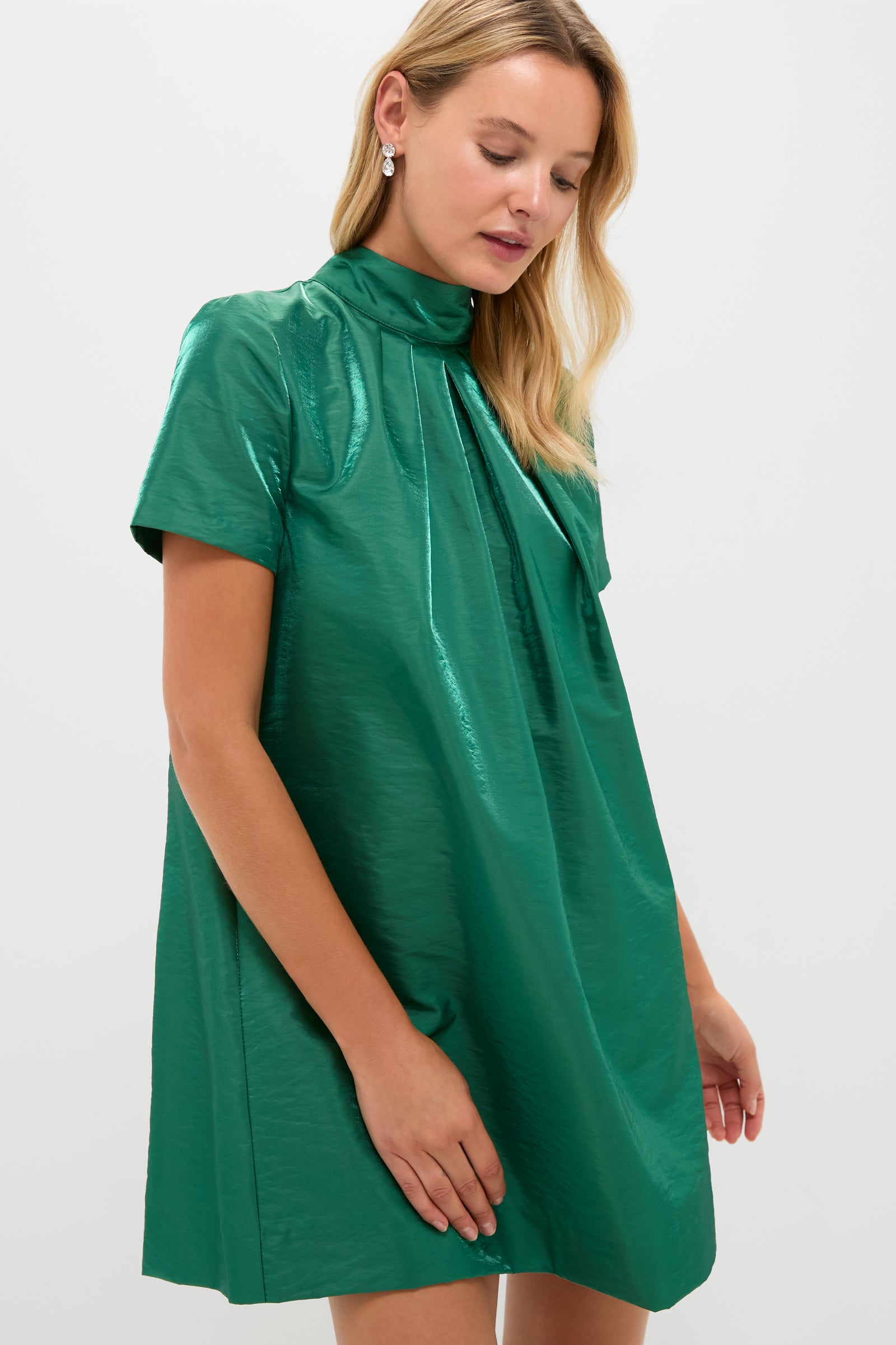 A woman wears a Hyacinth House shiny green taffeta dress with short sleeves and a high neckline, standing against a plain light background.
