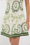 Person wearing the Ireland Green Layla Mini Dress, a classic, sleeveless cream dress with green botanical print and striped hem, exuding effortless charm and high-end style.