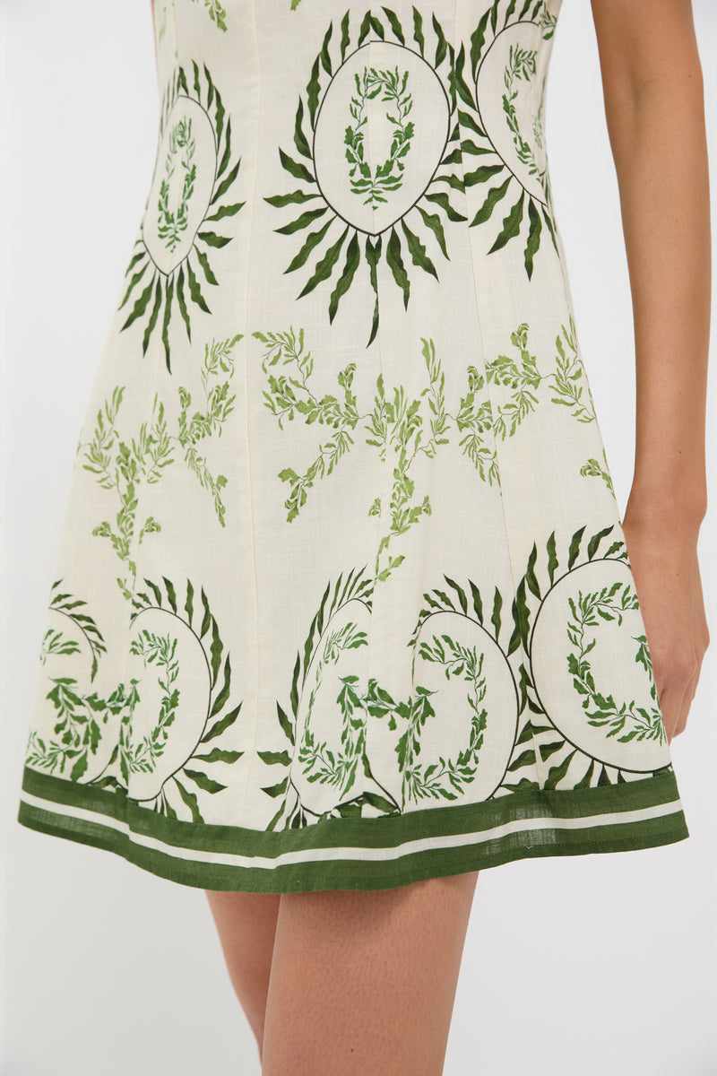 Person wearing the Ireland Green Layla Mini Dress, a classic, sleeveless cream dress with green botanical print and striped hem, exuding effortless charm and high-end style.