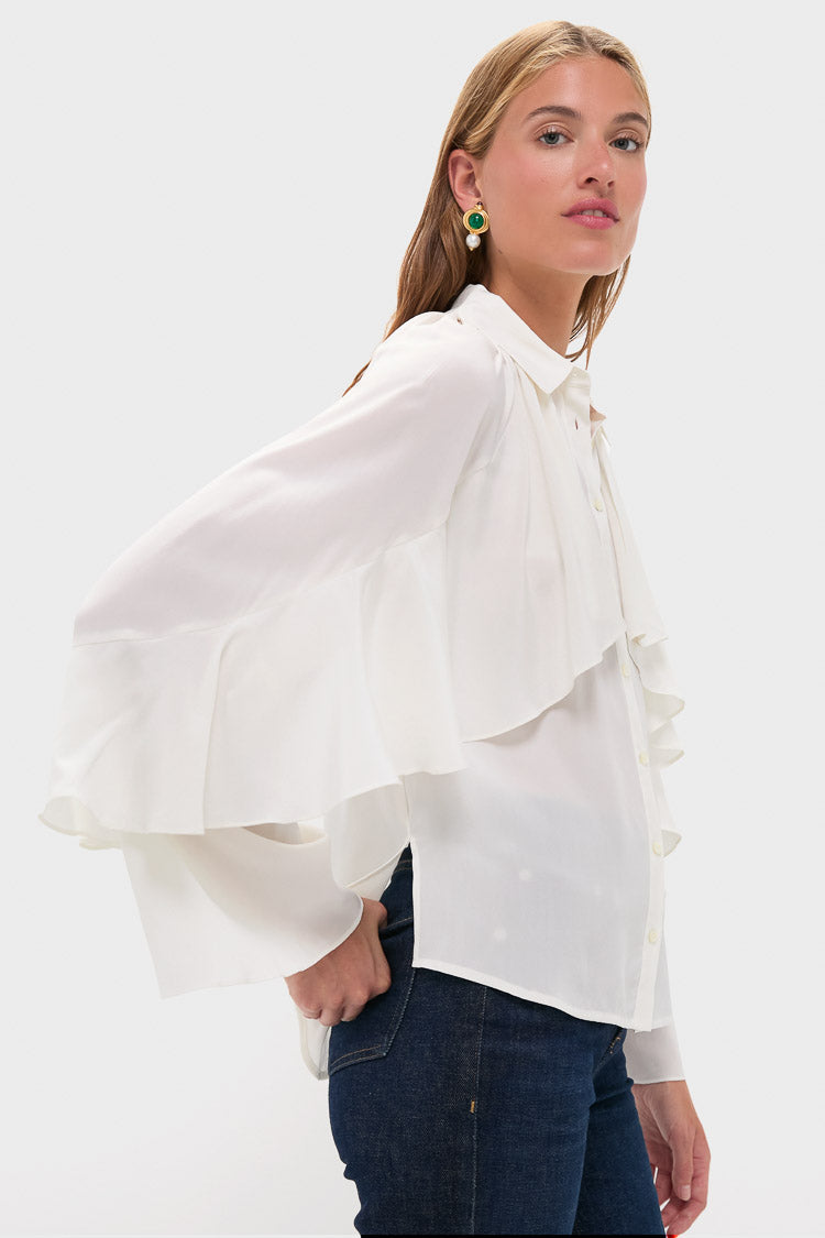 A woman models a Veronica Beard silk blouse with flared sleeves and ruffled details, paired with blue jeans, against a plain light background.