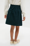 Child wearing classic Navy Douchka Skirt with heart-shaped pockets and elastic waist, paired with a cream sweater and glittery Mary Jane shoes. Effortless, fun, and high-end style.