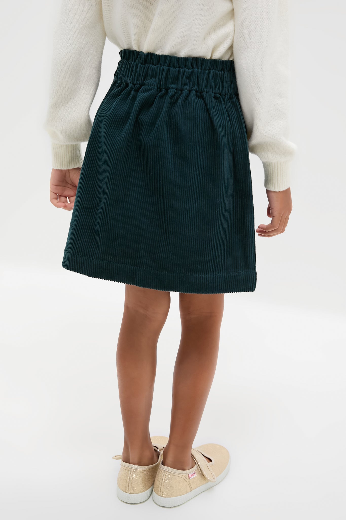 Child wearing classic Navy Douchka Skirt with heart-shaped pockets and elastic waist, paired with a cream sweater and glittery Mary Jane shoes. Effortless, fun, and high-end style.