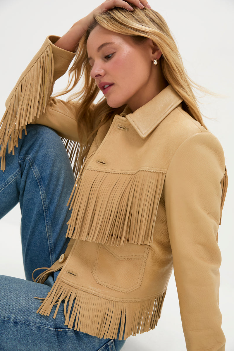 Woman wearing Tan Deerskin Fringe Jacket with a classic, effortless Western style; features swinging fringe trim and a shrunken fit, paired with blue denim jeans.