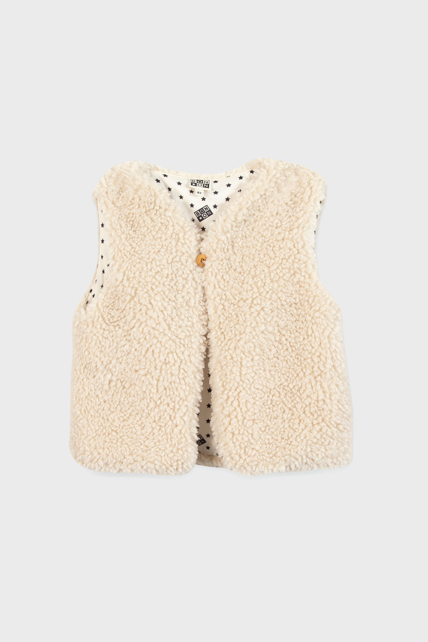 A sleeveless, cream-colored teddy vest by Bonton with a single front button and white lining adorned with small black stars—an ideal way to add Parisian chic to children’s outfits.