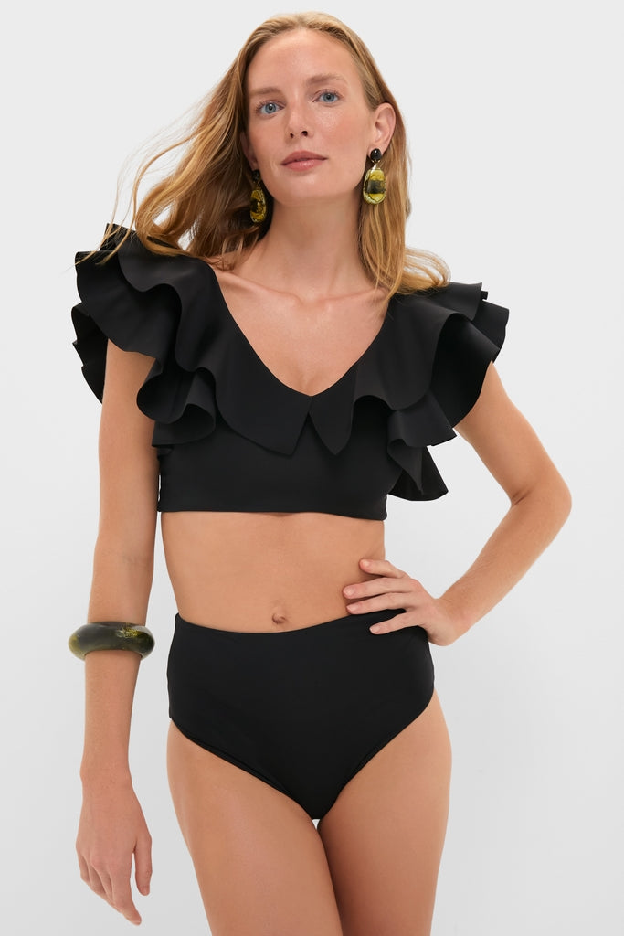 Model wearing the Black Mila Two Piece swimsuit featuring a classic V-neck with layered ruffle straps, high-waisted briefs, and accessorized with chunky resin-style earrings and bangle.