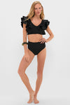 Model wearing Black Mila Two Piece swimsuit with ruffled bikini top and high-waisted bottoms, blending classic elegance and effortless style for a high-end, fun beach look.