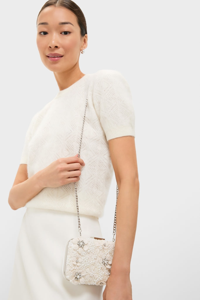 Young woman in a classic ivory ensemble holds the high-end Ivory Beth Encrusted Clutch, featuring crocheted flowers and silver crystals, radiating effortless elegance and fun.
