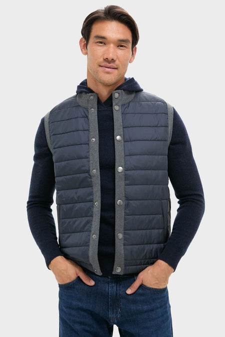 Male model wearing the classic Mid Gray Essential Gilet, a high-end, effortless sleeveless vest with a quilted front and snap closure, layered over a dark sweater.