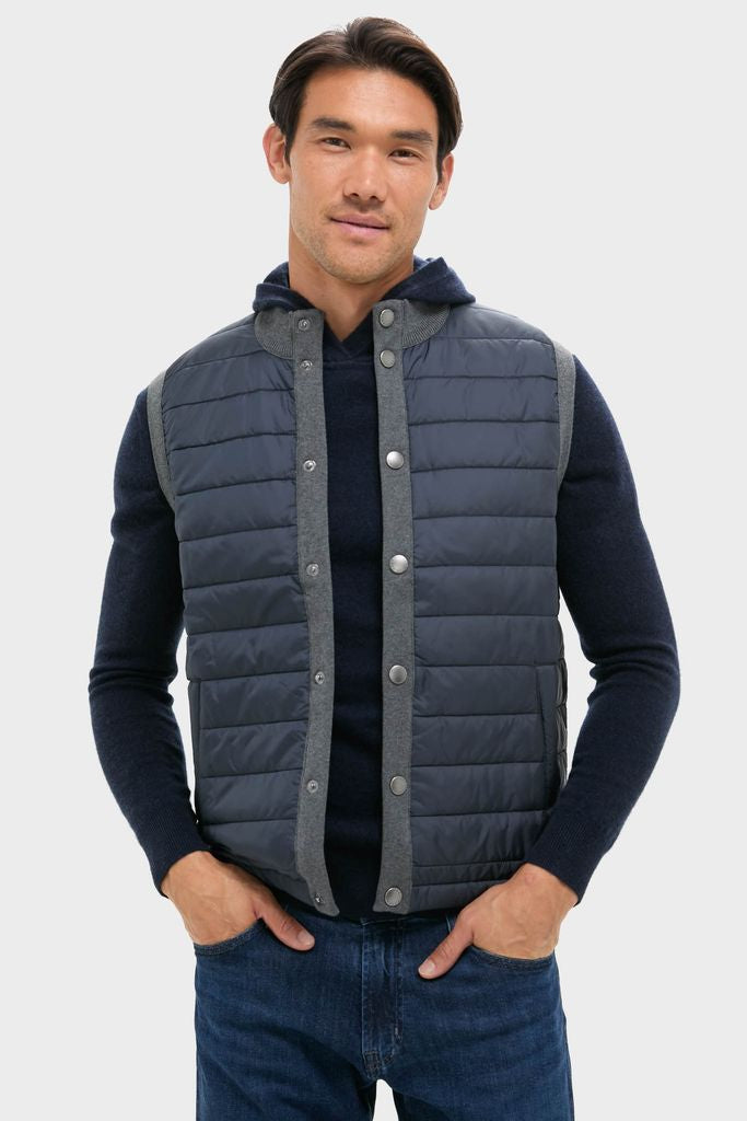 Male model wearing the classic Mid Gray Essential Gilet, a high-end, effortless sleeveless vest with a quilted front and snap closure, layered over a dark sweater.