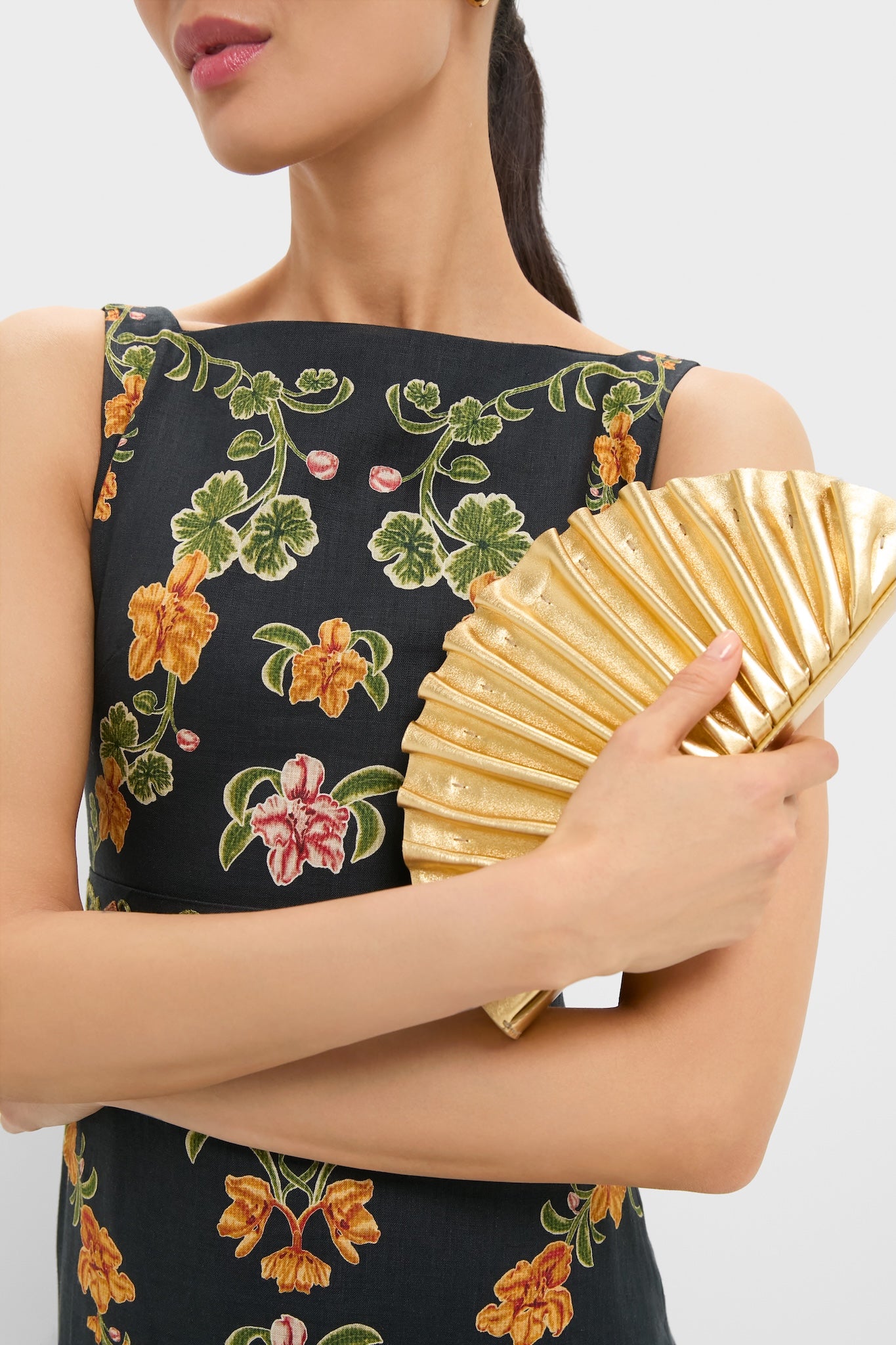 Woman holds the classic Gold Nala Mini Clutch, an effortless, high-end accessory with a fan silhouette, perfect for adding fun to any special occasion.