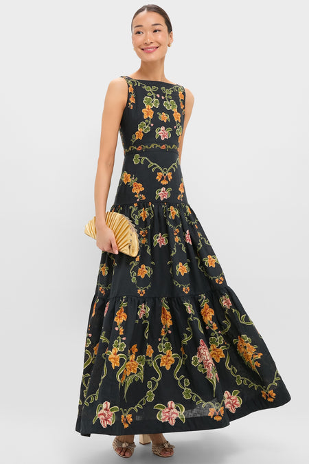 Woman elegantly showcases the Gold Nala Mini Clutch, a classic, high-end pleated bag. Effortlessly pairs with her floral maxi dress and open-toe heels for a fun, stylish look.