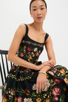 Woman seated wearing the Paramo Alcaparra Midi Dress, a classic, sleeveless piece with a fitted bodice and full skirt, featuring an effortless, high-end floral pattern.