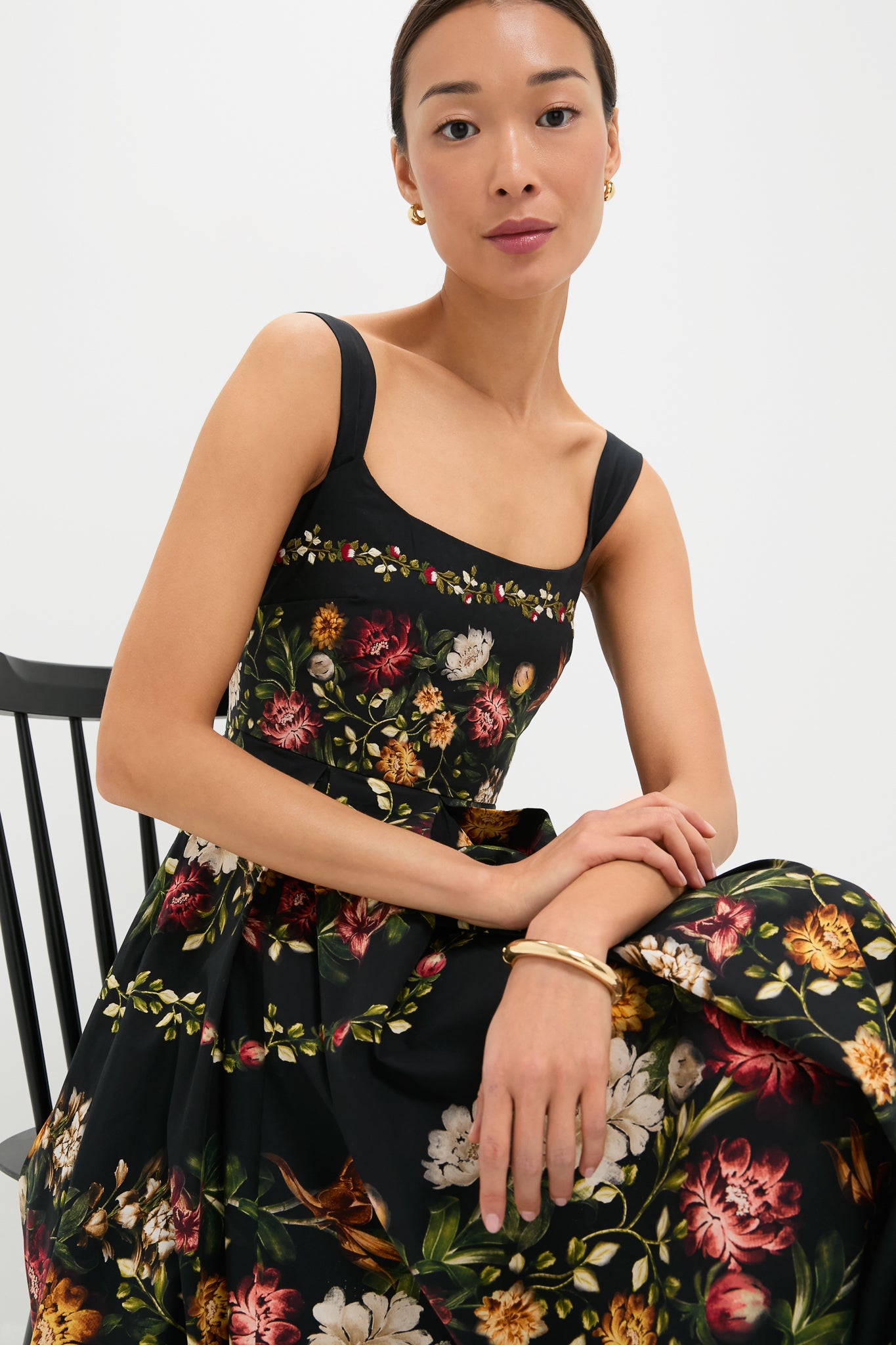 Woman seated wearing the Paramo Alcaparra Midi Dress, a classic, sleeveless piece with a fitted bodice and full skirt, featuring an effortless, high-end floral pattern.