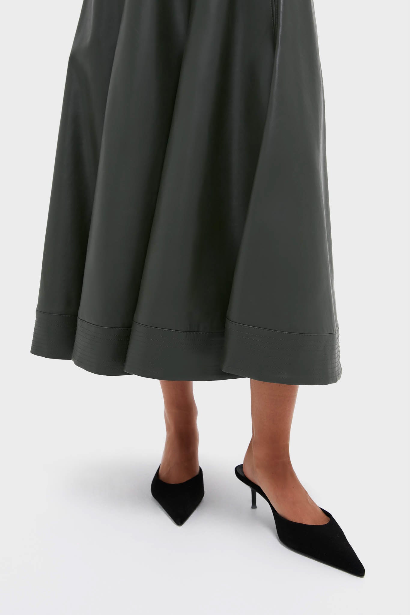 A person wearing a Tuckernuck maxi-length dark gray A-line skirt and black pointed-toe slingback heels stands against a plain white background.
