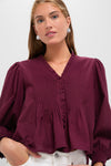 Young woman models the Exclusive Burgundy Anise Long Sleeve Top with pintuck pleats, puff shoulders, and smocked cuffs, paired effortlessly with light pants for a classic, high-end look.