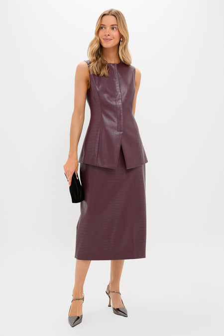 A woman poses against a plain background in a Tuckernuck sleeveless dark mauve textured top with a matching midi skirt, holding a black clutch and wearing silver pointed-toe heels.