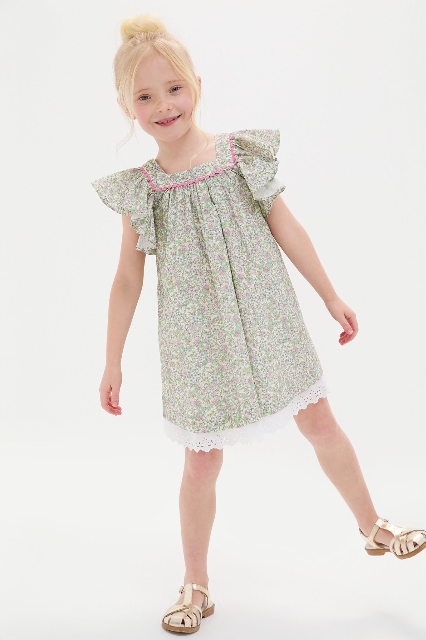 Young girl wears a green floral dress with ruffled sleeves and lace hem, paired with La Coqueta's Sofia Girl Sandals in Nappa leather.