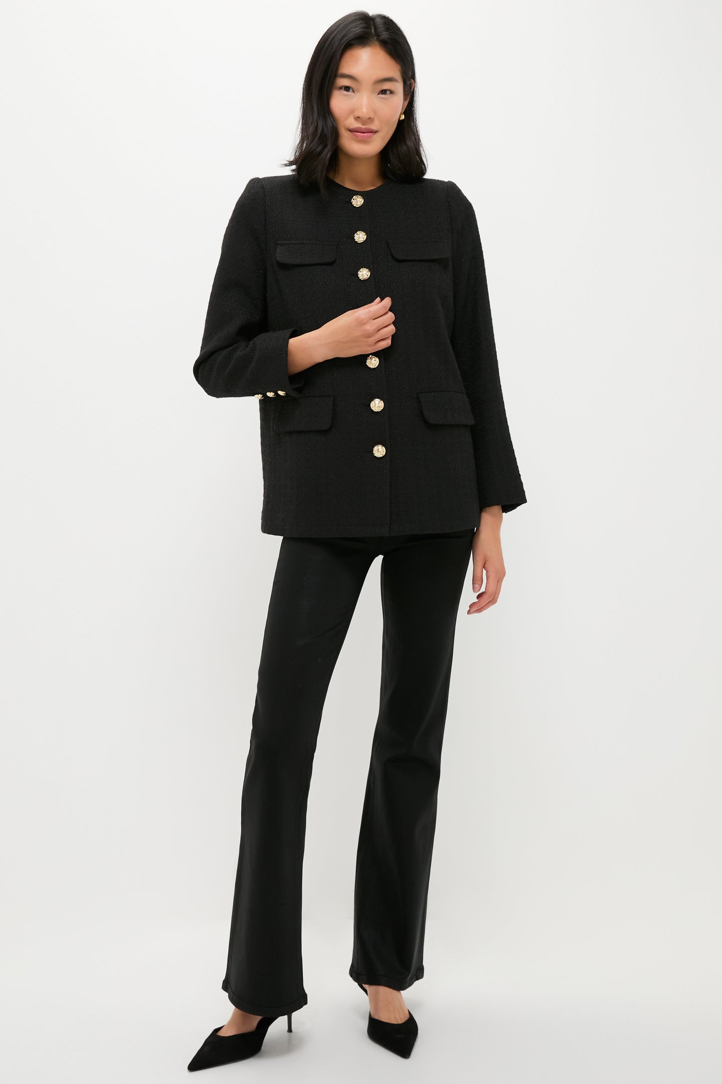 A woman stands against a white background wearing a black tweed blazer with gold buttons, black pants, and black heels by Pomander Place.