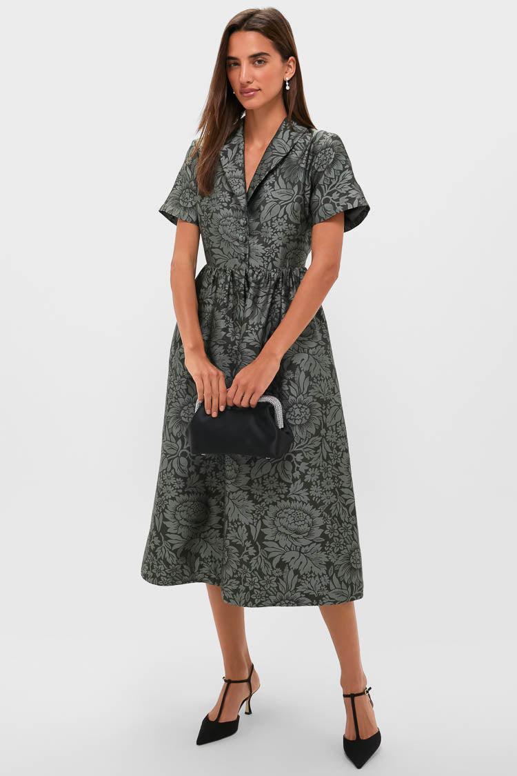 Female model in a classic Emerald Mirasol Jacquard Adelaide Dress with a defined waist, notched collar, and button-down front, styled with a black clutch and T-strap heels.