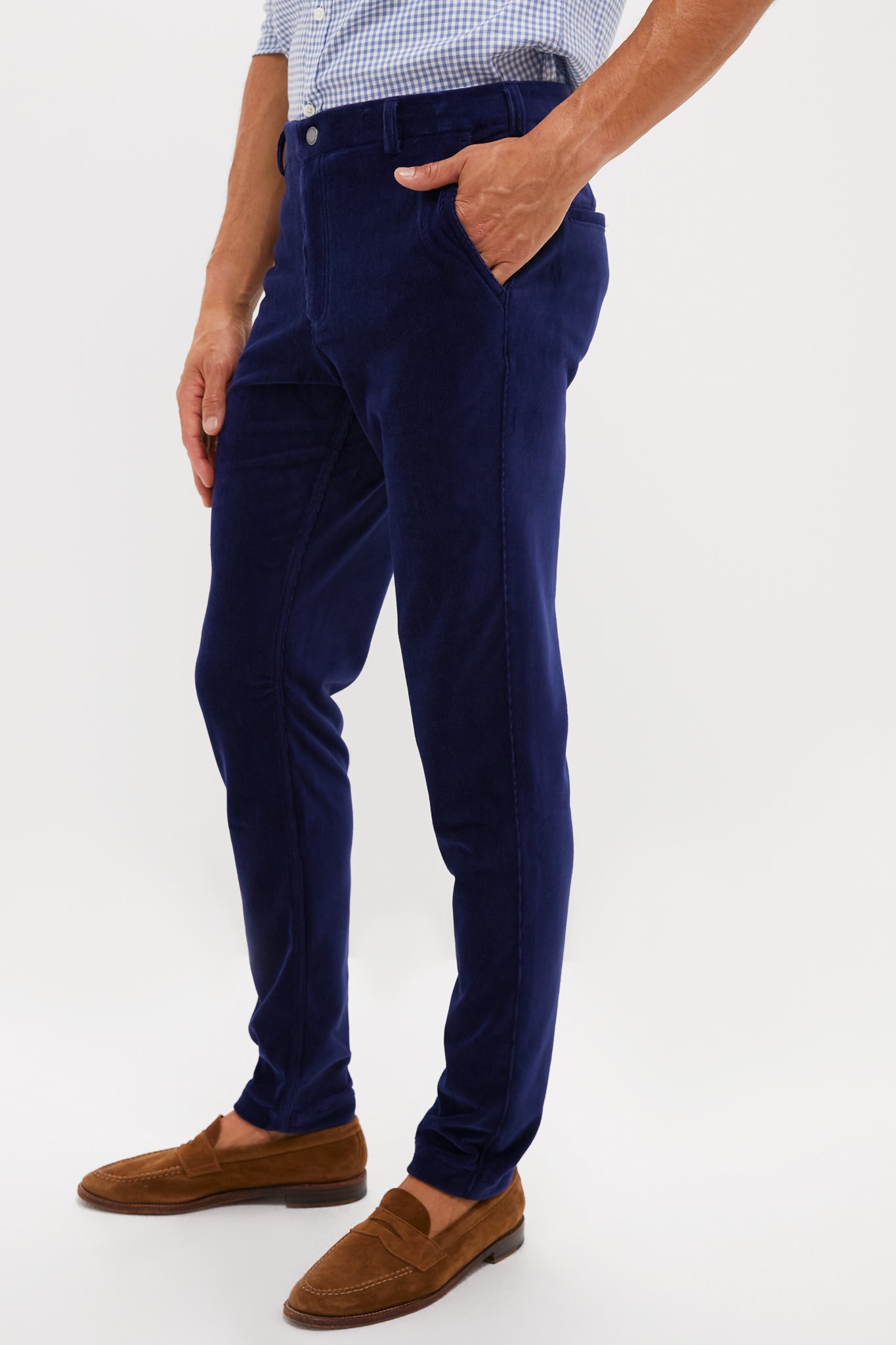 A man wearing REDVANLEY slim-fit performance corduroy trousers, a light blue checkered shirt, and brown suede loafers stands with one hand in his pocket.