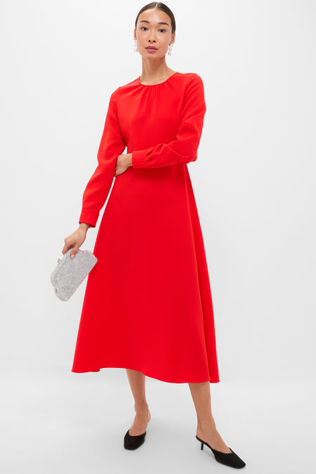 Woman wearing the classic Red Delancey Dress, featuring a round neckline and full skirt, holding a sparkly clutch, embodying effortless elegance for high-end, fun occasions.