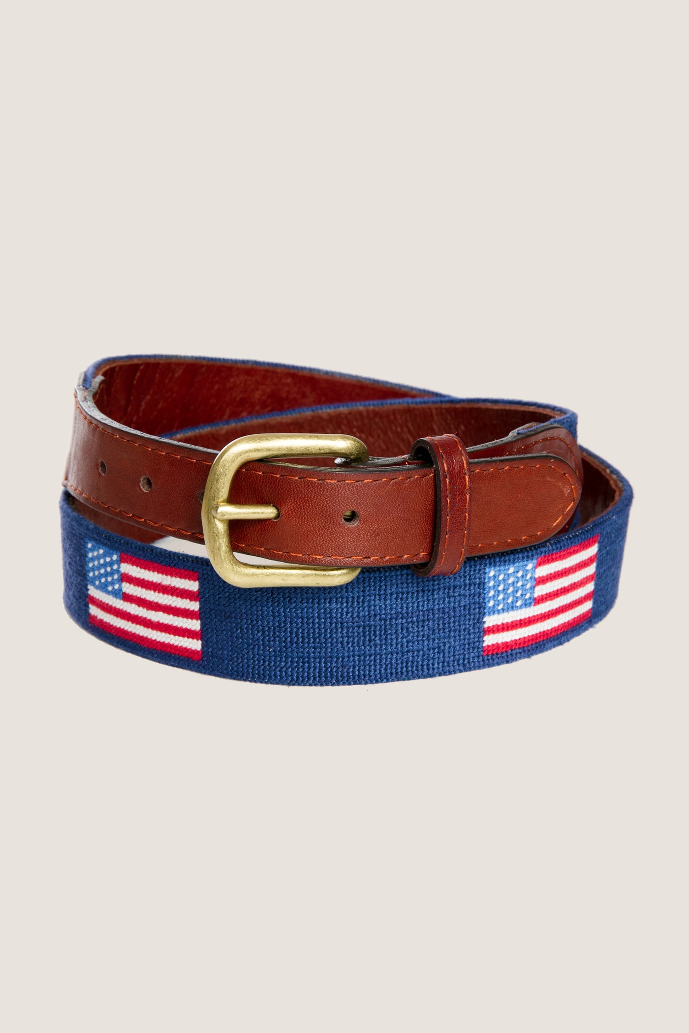 American Flag Needlepoint Belt with classic U.S. flag motifs on blue needlepoint fabric, brown leather trim, and brass buckle, offering an effortless and fun high-end style.