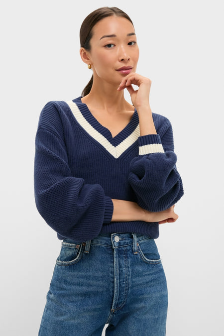 A woman models the Washed Navy Ashe Sweater, showcasing its classic V-neck, balloon sleeves, and effortless tuck into high-waisted jeans, embodying high-end, fun style.