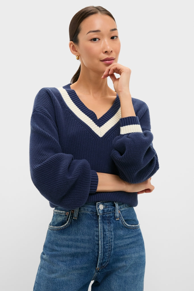 A woman models the Washed Navy Ashe Sweater, showcasing its classic V-neck, balloon sleeves, and effortless tuck into high-waisted jeans, embodying high-end, fun style.